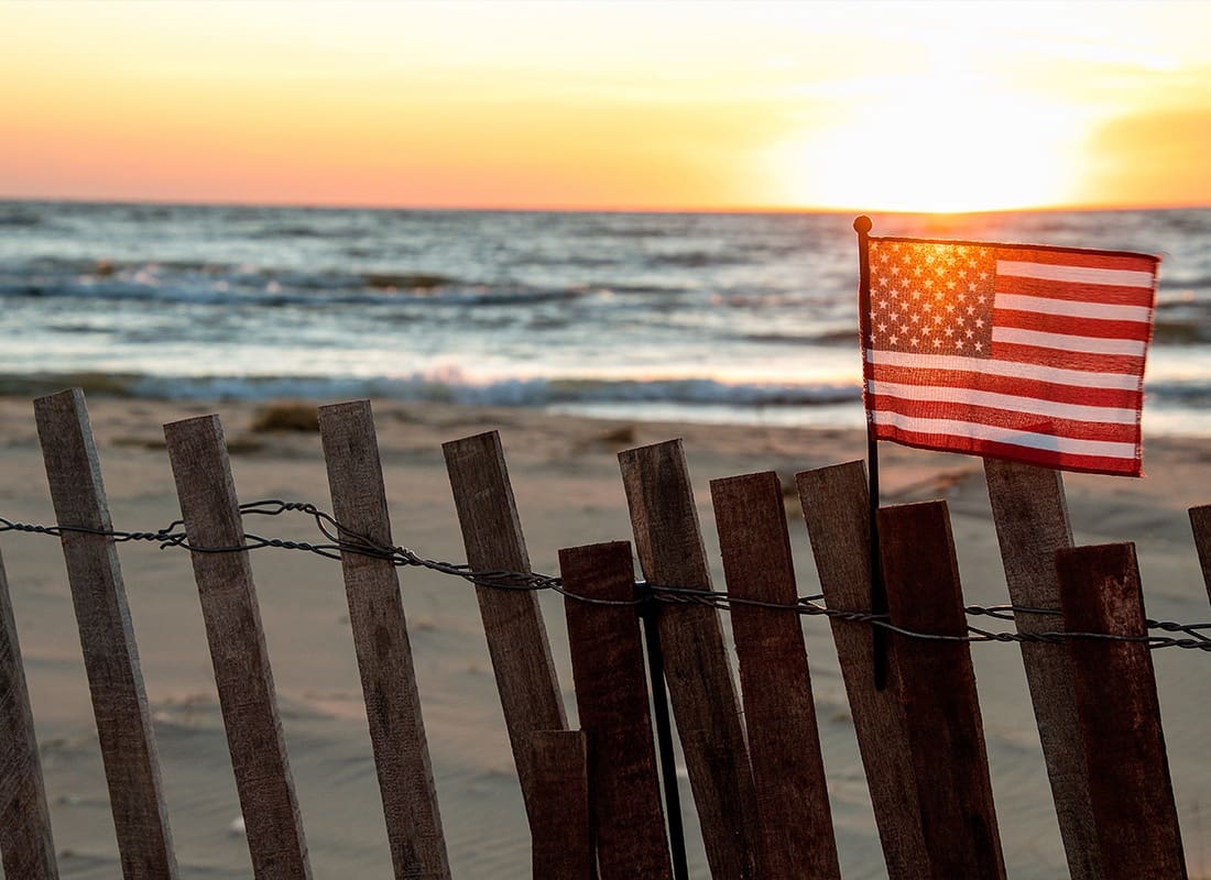 About Our Agency - Sunset Illuminating American Flag on Beach Fence With Lake Michigan Background